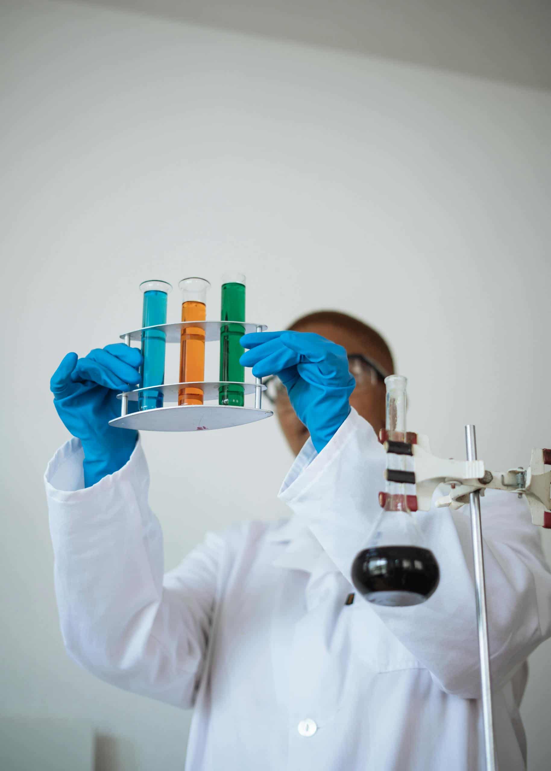 Unrecognizable African American chemist wearing uniform and analyzing chemical reaction while holding stand with test tubes in hands in modern lab